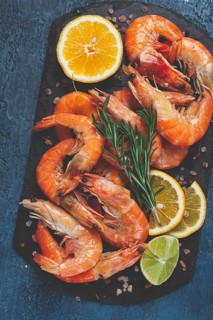 Freshly frozen shrimp, with lemon and rosemary, on black slate, close-up, top view, no people