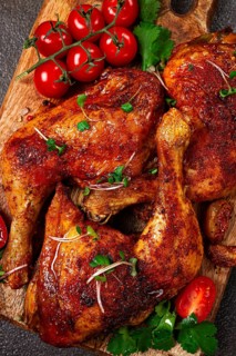 Grilled fried chicken legs, served with fresh cherry tomatoes, and herbs, on a wooden chopping