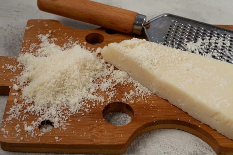 Freshly sliced and grated cheese, parmesan cheese, Gran gusto. Grana padano. on a wooden chopping
