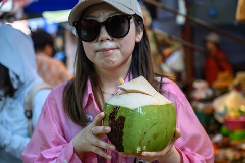 Mae Klong, Thailand. March 15th 2025. A smiling tourist with fresh coconut juice at the Mae Klong