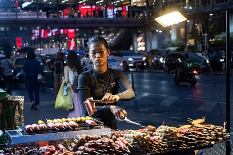 Bangkok, Thailand. March 26th 2025. A Thai woman cooks grilled meat at a street food stall at night