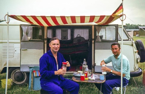Two men having breakfast at campsite sitting outside a VW Volkswagen camper van vehicle, 1971