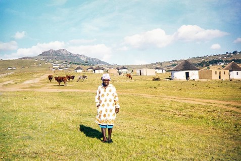A local woman stands in the foreground of a rural Xhosa village (umuzi) in the Eastern Cape, South