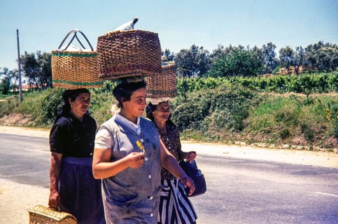 Three women walking on street in rural area carrying wicker baskets on their head, Portugal, Europe