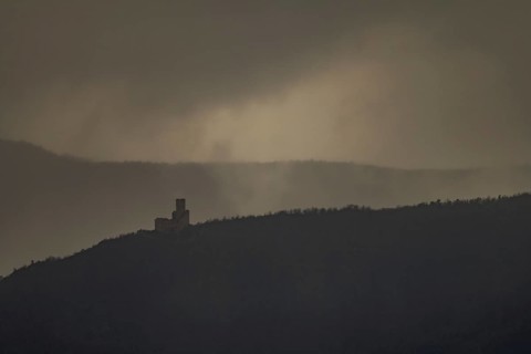 The structure is on a mountain. The sky is cloudy and sunlight is shining in the distance. The