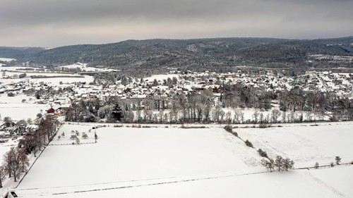 Aerial view of a snowy landscape with fields, hills and a village under grey sky, Herleshausen in