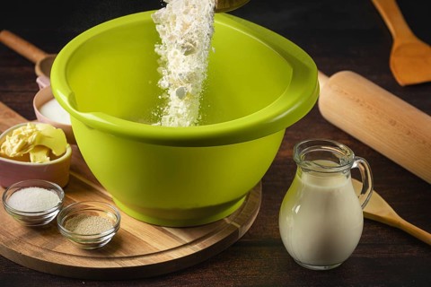 Flour falls into a green bowl surrounded by baking ingredients
