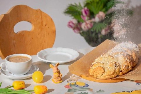 Yeast braid is sprinkled with sugar, breakfast table with coffee and decoration for Easter