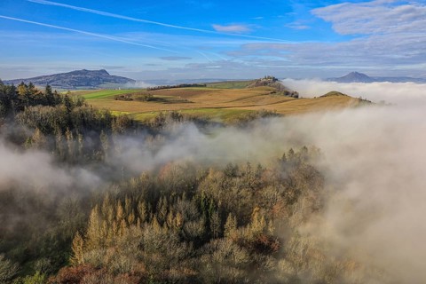 Foggy landscape in Hegau with hills and forests under a clear blue sky, Hohenkrähen castle ruins,