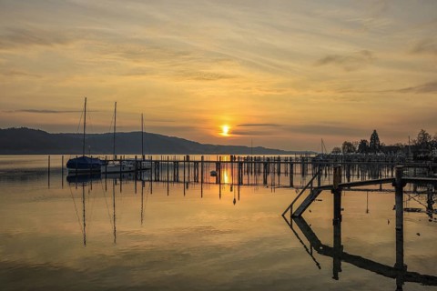Atmospheric sunrise scene with calm water and sailboats on the jetty, Lake Constance, Überlinger
