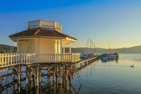 A pavilion on a jetty stretches across Lake Überlingen, with boats and mountains in the background