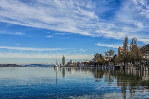 Calm lake in winter with a sailboat on the shore, surrounded by houses and trees, under a cloudy
