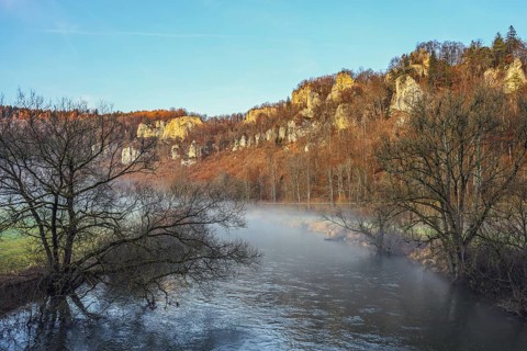 Picturesque river landscape with foggy water, surrounded by autumn trees and imposing Jurassic