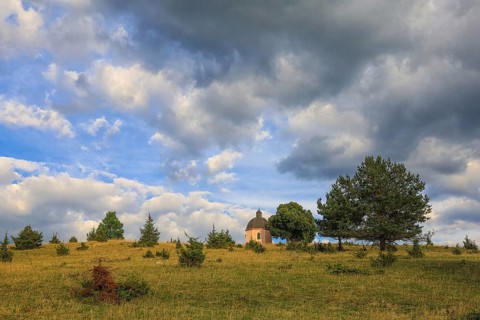 A small chapel stands on a green hill under a cloudy sky with trees, Upper Danube nature park Park,