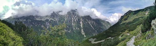 A trail leads through impressive mountain scenery, panoramic peaks covered with green slopes and