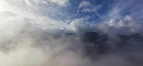 Atmospheric scene with clouds and fog over a mountain landscape under blue sky, hiking in the High