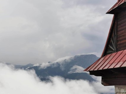 View of a mountain peak through clouds, with part of a wooden building in the foreground, Zakopane,