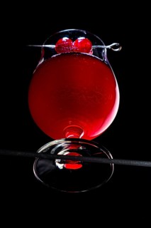 A cognac glass with red liquid and cherries, dramatically illuminated, view from below