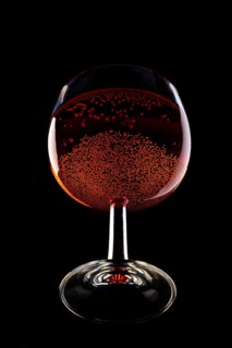 A wine glass filled with sparkling red wine against a black background