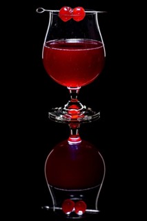 Red drink in a cognac glass with cherries against a dark background and reflection