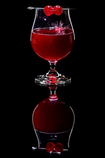 Cherry falls splashing into a cognac glass with a red drink against a dark background and