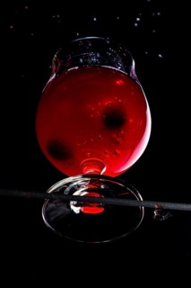 Cherries fall into a cognac glass with red liquid, dramatically illuminated, view from below