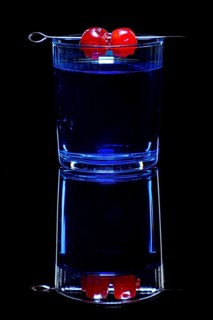 Blue drink in a glass with cherries, against black background and reflection