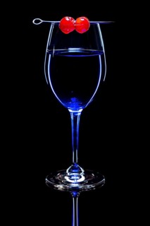 Blue drink in a wine glass with cherries, black background and reflection