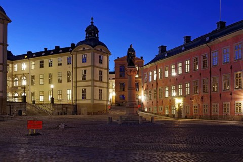 An illuminated town square with historic buildings and a memorial at dusk, Riddarholmen, Stockholm,