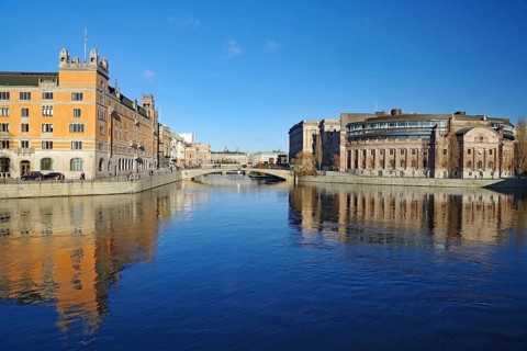Clear river water with reflecting buildings and a bridge under a blue sky, Government District,