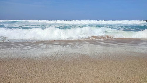 Empty sandy beach with breaking waves under clear blue skies, hiking on the Fisherman's Trail,