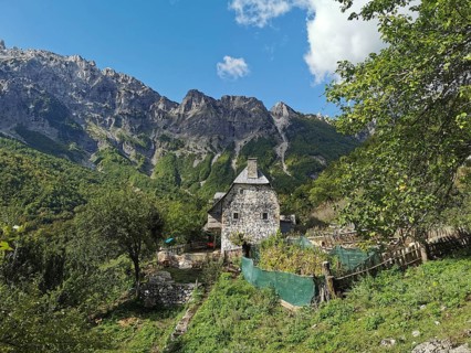 Stone house surrounded by gardens and mountains under a clear blue sky, Peaks of the Balkans,
