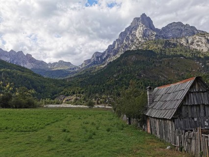 Small wooden cabin in a grassy willow with majestic mountains in the background, Peaks of the