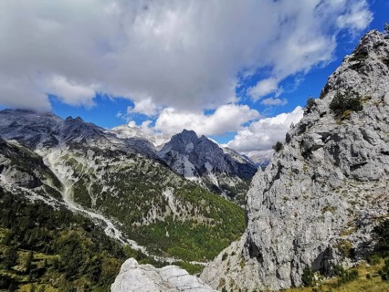 Rugged mountain landscape with clouds and blue sky, trees on rocky hillside, Peaks of the Balkans,