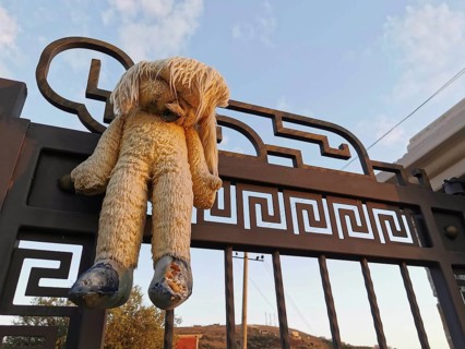 An old plush bear hangs abandoned on a rusty, metal gate at dusk, Himare, Albania