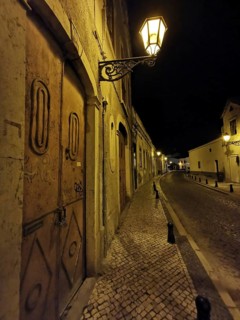 Night view of a lonely paved street with cozy glowing lanterns and historic buildings, Faro,