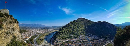 Panorama, view of a castle on a hill with Albanian flag with river and city in the valley under a