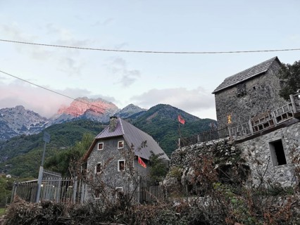 Traditional village with stone houses and Albanian flags against a mountain backdrop, mountain