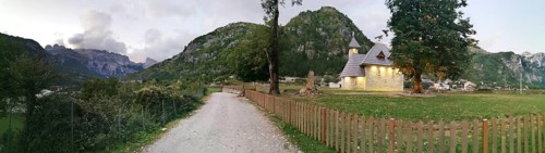 Picturesque church in Theth, a village with mountains in the background and a garden fence, Peaks