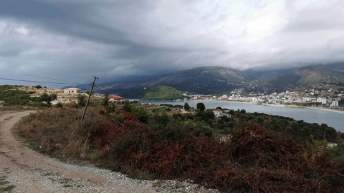 Hilly coastal landscape with a path by the sea and a village on a mountainside under cloudy sky,