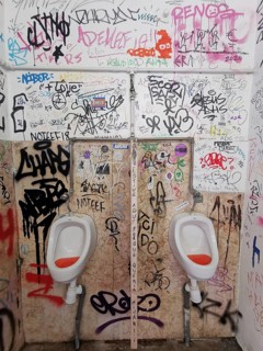 Public restroom area with graffiti-decorated walls and two urinals, Lisbon, Portugal