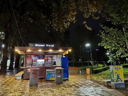An illuminated sausage stand, Wiener Wurst, at night in a wet park, Tirana, Albania