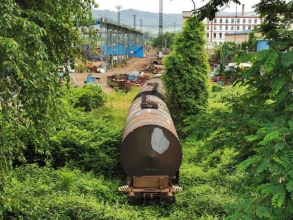 An old, rusted freight train in an industry-like setting surrounded by lush greenery, Czech
