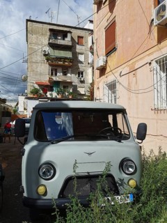 Old van, UAZ Buchanka, in front of colorful residential buildings on a sunny city street in Tirana,
