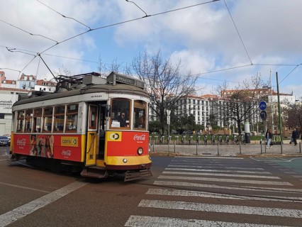 A yellow and red historic tram runs through the city under a cloudy sky, Lisbon, Portugal