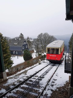 Red train goes through snow-covered mountain landscape, Oberweissbach cable car, Rennsteig,