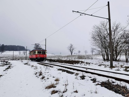 A red train travels through a snow-covered landscape, snow-covered fields in the background,