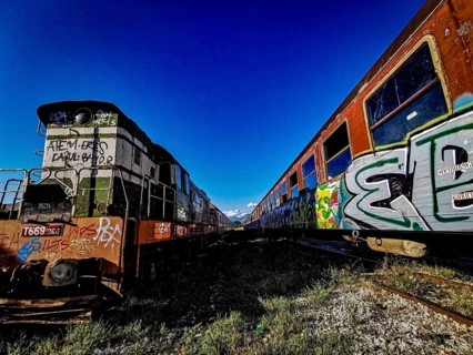 Train front painted with colorful graffiti, next to another painted train, Albania