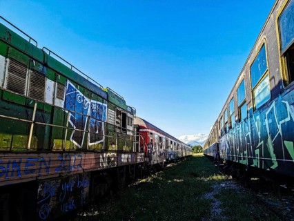Two painted trains under a bright blue sky on abandoned tracks