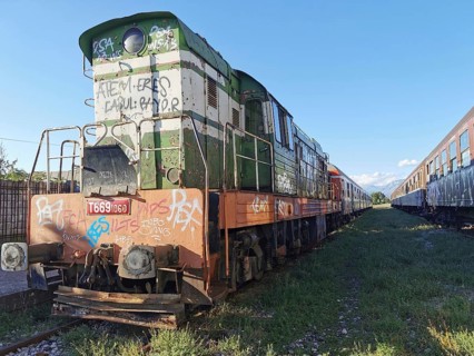 Graffiti-painted locomotive on rails, other abandoned trains next to it, Albania